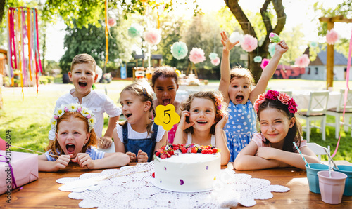 Konstfotografi Children with cake standing around table on birthday party in garden in summer