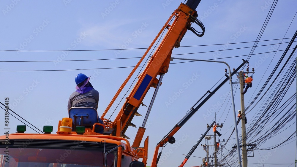 Electricians team with crane trucks are working to install electrical systems on electric power poles against blue sky background, focus on electrical driver controlling crane on foreground