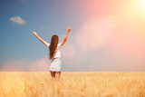 Happy woman enjoying the life in the field Nature beauty, blue sky, bright sun and field with golden wheat. Outdoor lifestyle. Freedom concept. Woman jump in summer field