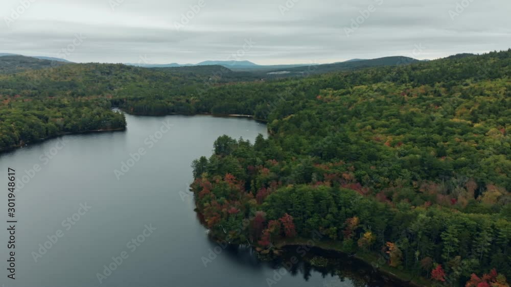 Foliage Season in Maine, New England - Smooth aerial rotation showing a lake in the middle of a romantic forest surrounded by green trees, red trees, and orange trees on a cloudy day Foliage Season in Maine, New England - Smooth aerial rotation showing a lake in the middle of a romantic forest surrounded by green trees, red trees, and orange trees on a cloudy day