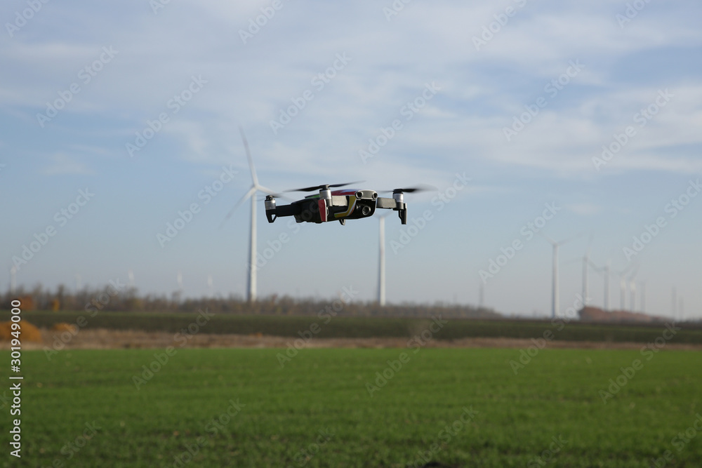 Fototapeta premium quadcopter drone in flight against the background of wind turbines in the field. New technology concept. Agricultural complex