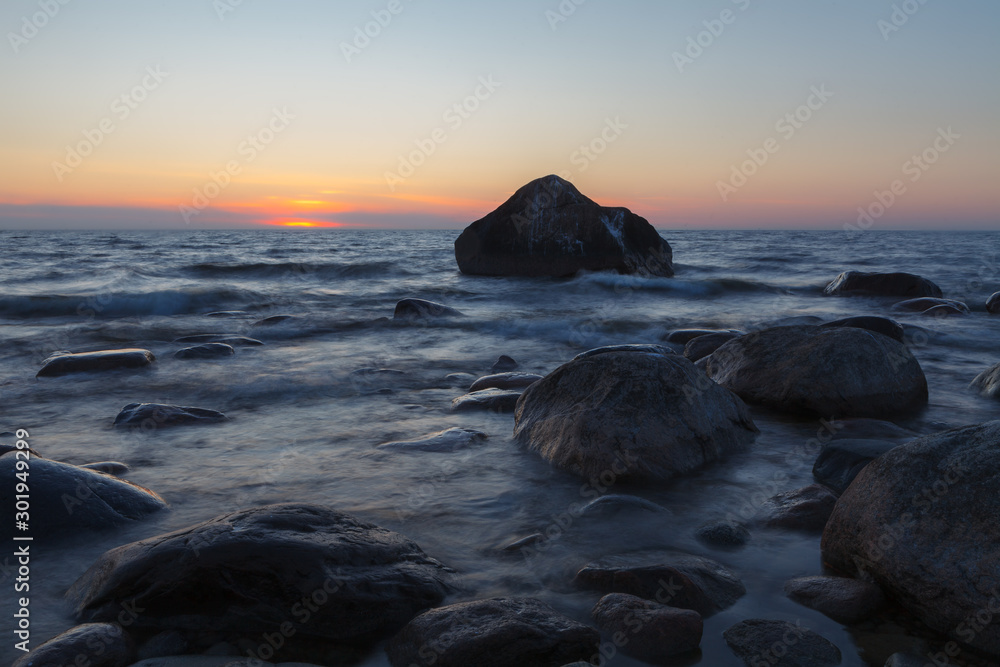 Sunset over silhouettes of stones and boulders laying on a shore. Long exposure
