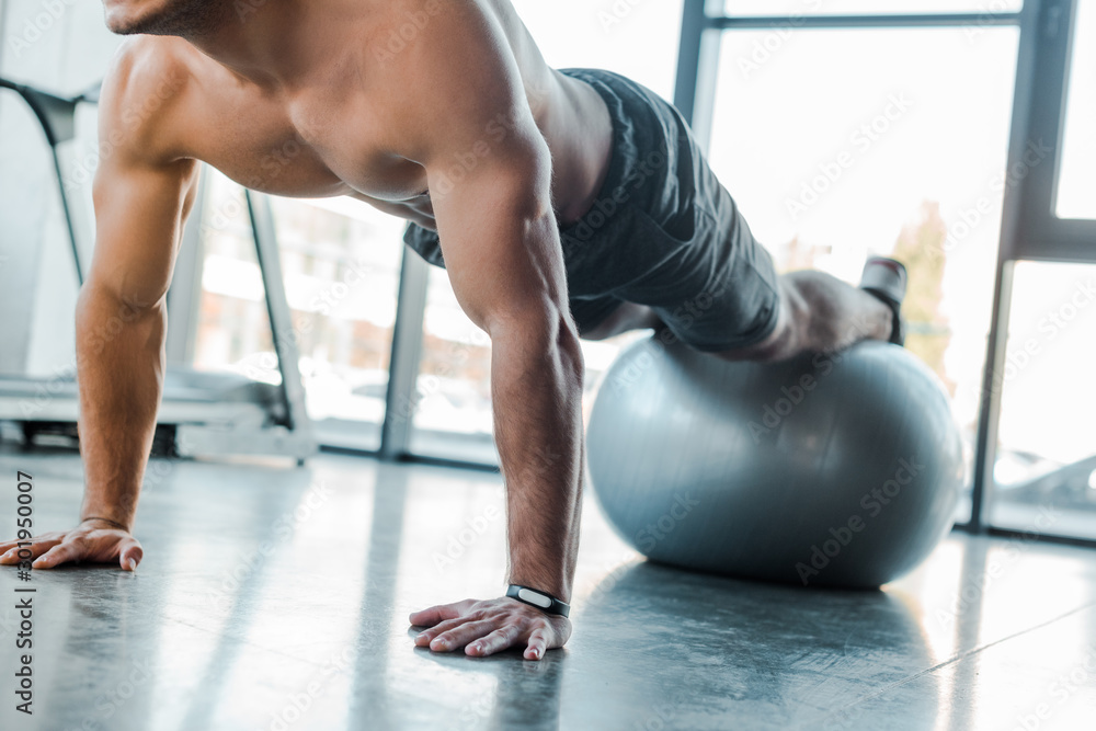 cropped view of handsome sportsman doing plank on fitness ball in sports center cropped view of handsome sportsman doing plank on fitness ball in sports center