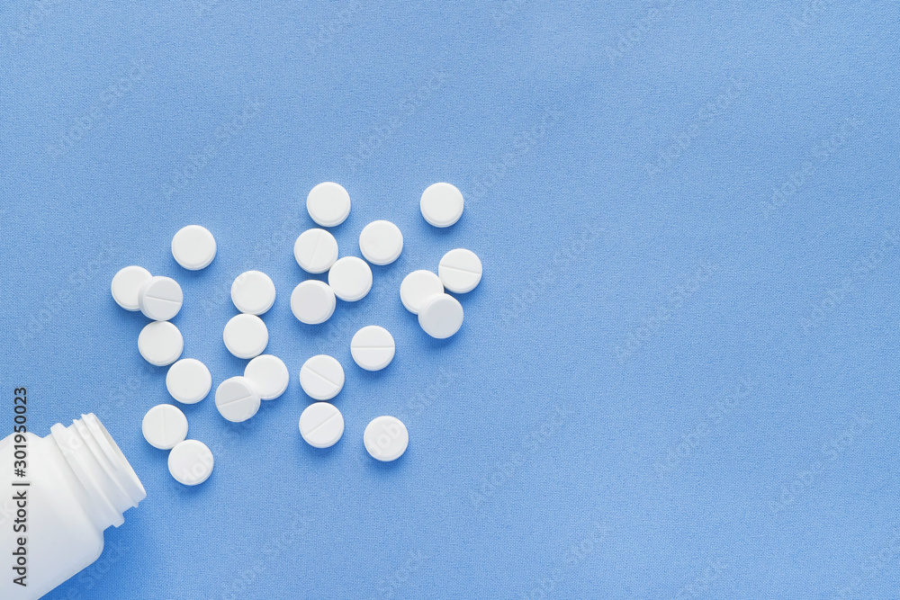 Bottle with white vitamin pills scattered on a blue background. Bottle with white vitamin pills scattered on a blue background.