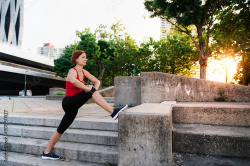 Young woman doing exercise outdoors in city at sunset, stretching. © Halfpoint