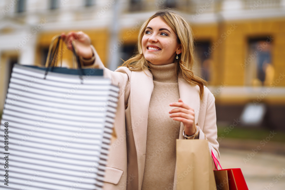Beautiful girl holds out multi-coloured bags with purchases. Young woman holding shopping bags on the city street. Consumerism, shopping, sales, lifestyle concept. Black friday. Beautiful girl holds out multi-coloured bags with purchases. Young woman holding shopping bags on the city street. Consumerism, shopping, sales, lifestyle concept. Black friday.