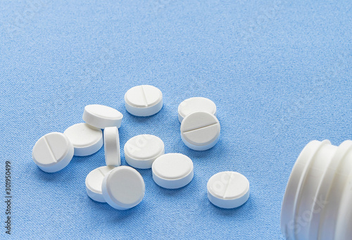 Bottle with white vitamin pills scattered on a blue background.