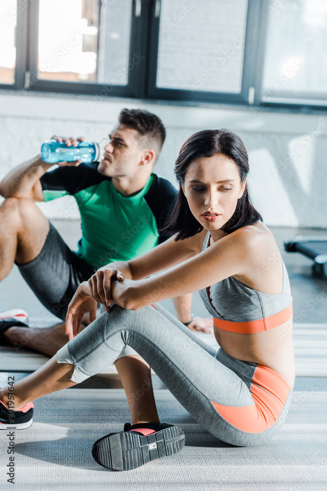 Obraz premium sportsman drinking water and sportswoman sitting in sports center
