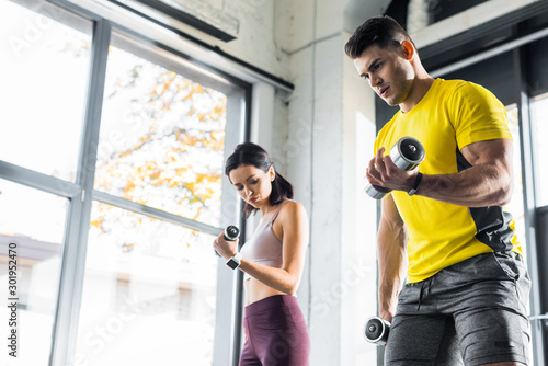 sportsman and sportswoman working out with dumbbells in sports center