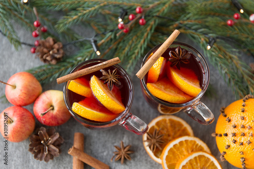 christmas and seasonal treats concept - glass of hot mulled wine with orange slice, apples and fir branch on grey background