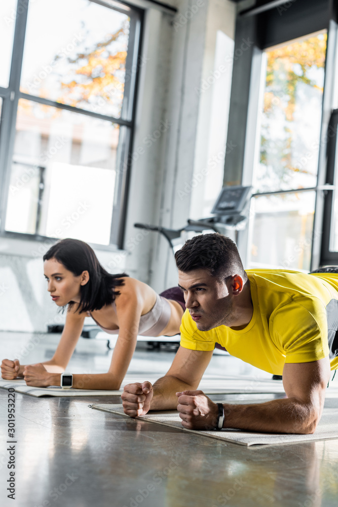 Obraz premium sportsman and sportswoman doing plank on fitness mats in sports center