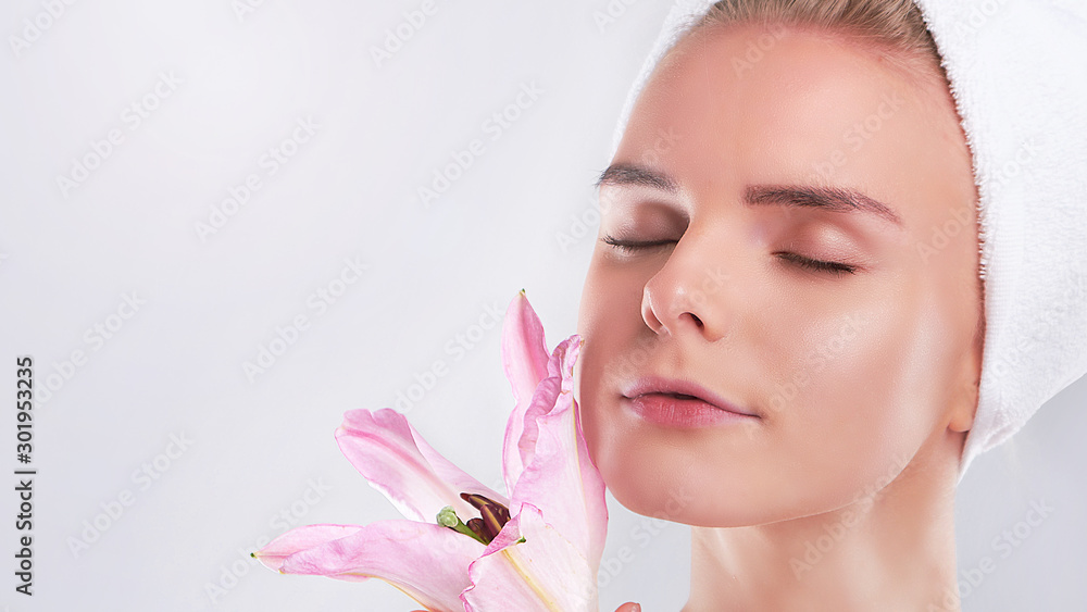 Fototapeta premium Young Woman with Clean Fresh Skin. Beautiful young girl. Photo of blonde girl with Lily on grey background. Skin care concept