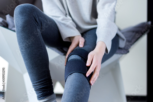 Closeup female leg in grey leggings dressed in knee brace to help promote recovery of bones, muscles, ligaments. Woman is feeling pain in joints after injury. Arthritis and meniscus diseases concept. photo