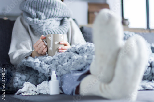 Fotografie, Obraz Sick girl in scarf and knitted socks is sitting in bed sofa wrapped in grey blanket