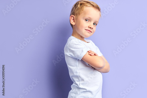 Side view on cute little boy posing isolated over purple background, looking at camera. Portrait photo