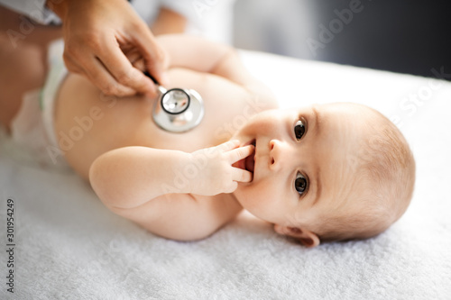 medicine, healthcare and pediatrics concept - close up of female doctor with stethoscope listening to baby girl's patient heartbeat or breath at clinic or hospital photo