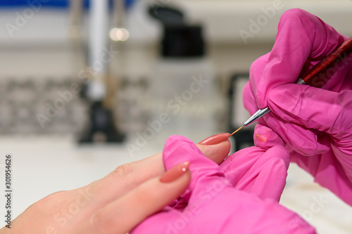 А manicurist in pink gloves processes the nails of an adult client using a variety of equipment. Manicure. Beauty shop. Gloved hands take care of the nails of the hands. Procedures.
