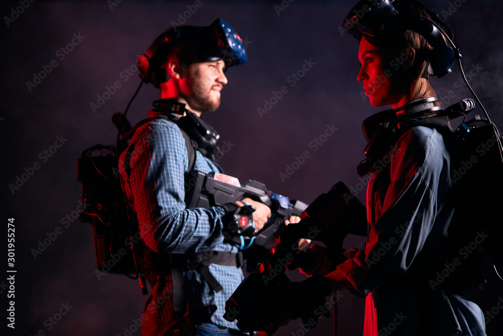 Young couple or friends stand and look in opposite sides, ready to fight. Virtual reality games, concept. Smoky UV background Young couple or friends stand and look in opposite sides, ready to fight. Virtual reality games, concept. Smoky UV background