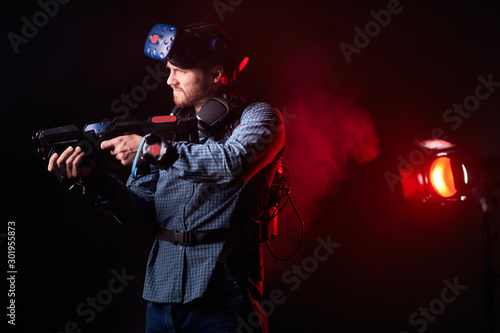 Portrait of young man holding VR weapon, wearing casual clothes playing virtual game. Isolated over smoky background