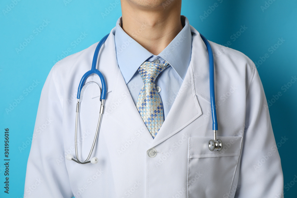 Doctor in medical gown with stethoscope against blue background, close up Doctor in medical gown with stethoscope against blue background, close up