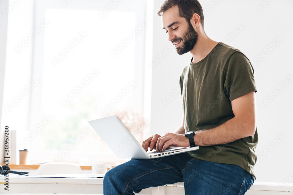 Image of handsome focused man typing on laptop and smiling