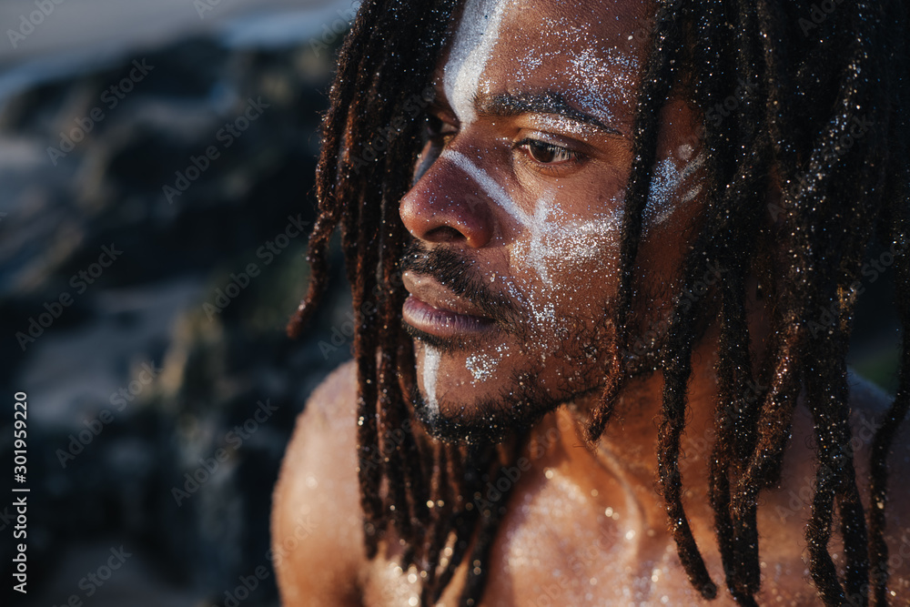 Outdoor emotional Fashion Portrait of African man wearing long dreadlocks and fancy makeup white face paint - obrazy, fototapety, plakaty 
