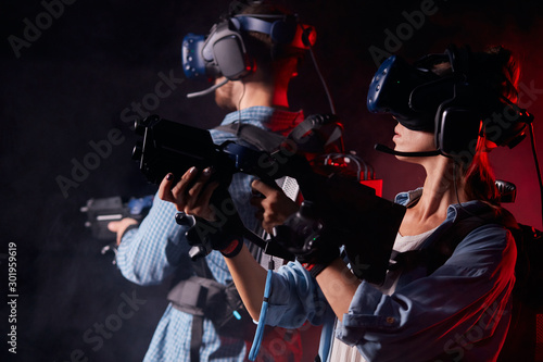 Caucasian man and woman stand holding virtual guns and wearing goggles, in casuan clothes. innovation future, fiction, vr