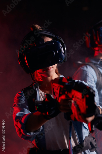 Young girl hold vr weapon standing in smoky isolated space, neon backlit