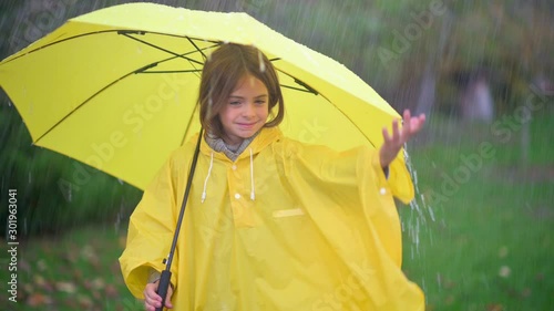 Cute little girl with a yellow umbrella in the rain. A child in a raincoat catches raindrops. Rainy weather.