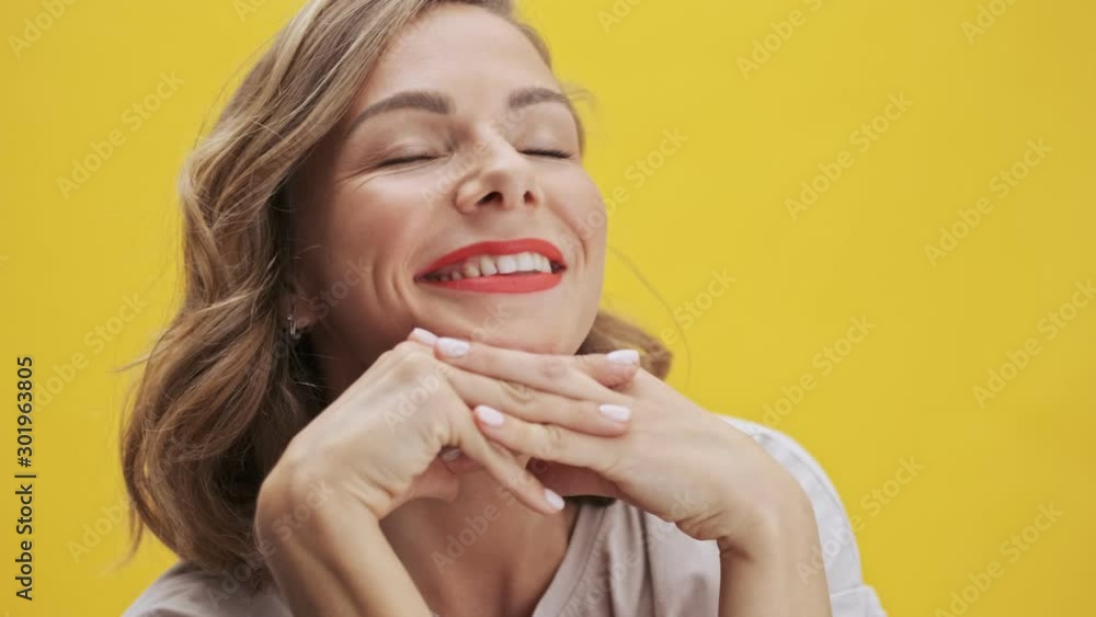Happy young woman with red lips smiling and dreaming while looking up and at the camera over yellow background isolated Happy young woman with red lips smiling and dreaming while looking up and at the camera over yellow background isolated