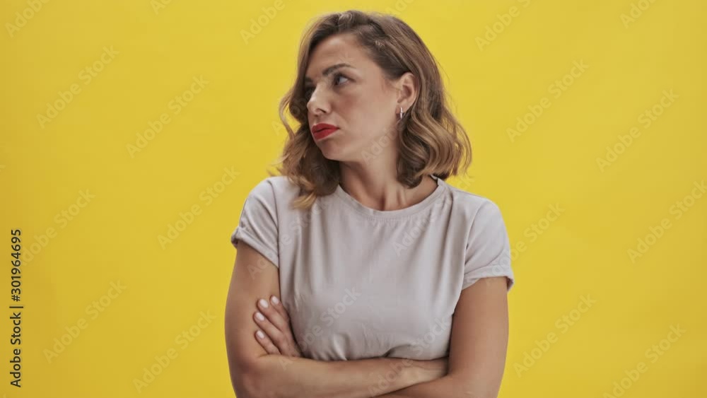 Displeased young woman with red lips staying with crossed hands on her body that shows how she is unhappy looking at the camera over yellow background isolated Displeased young woman with red lips staying with crossed hands on her body that shows how she is unhappy looking at the camera over yellow background isolated