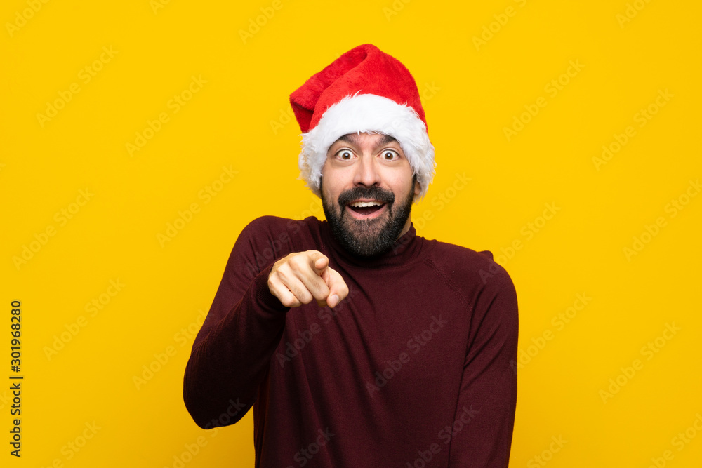 Man with christmas hat over isolated yellow background surprised and pointing front Man with christmas hat over isolated yellow background surprised and pointing front