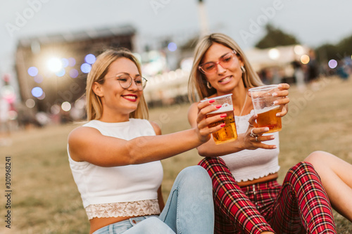 Girls sitting on the ground and cheering with beer at music festival