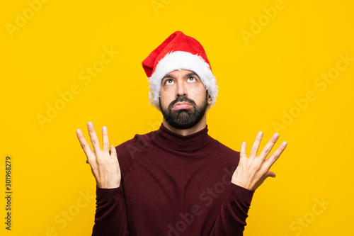 Man with christmas hat over isolated yellow background frustrated by a bad situation © luismolinero