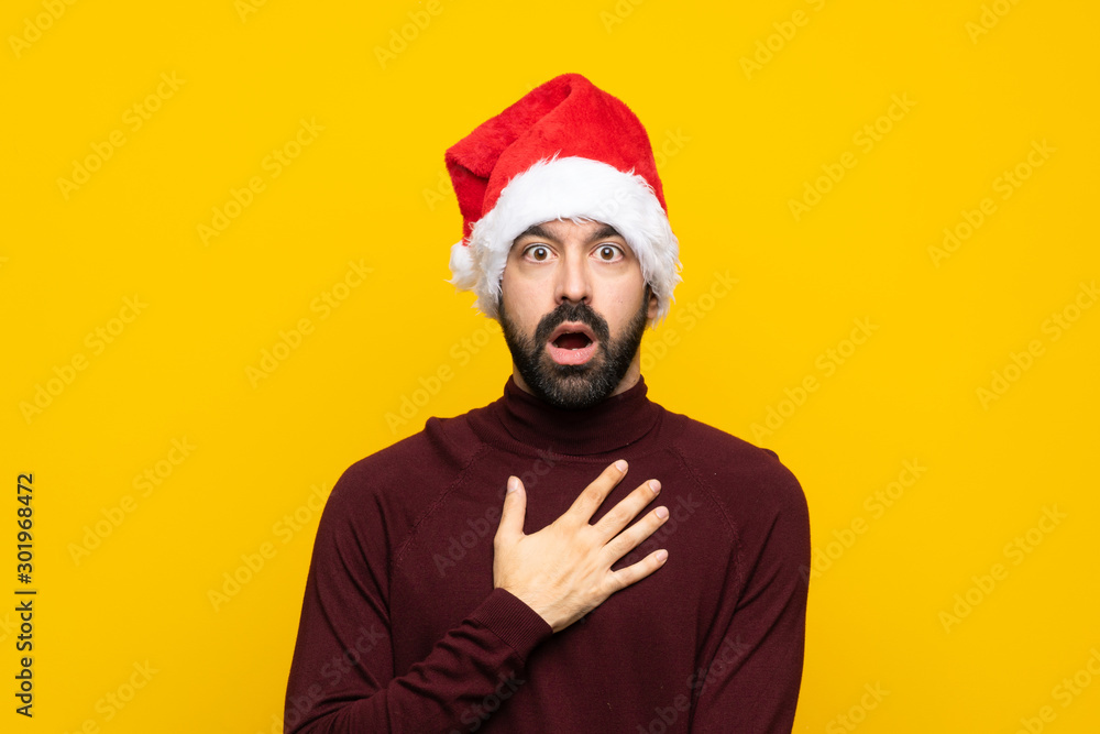 Man with christmas hat over isolated yellow background surprised and shocked while looking right Man with christmas hat over isolated yellow background surprised and shocked while looking right