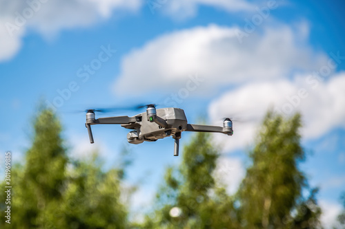 A gray drone flies against the sky and trees.