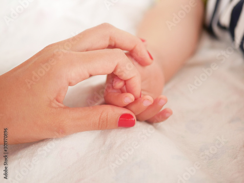 Mom holds the hand of a newborn baby. Close-up. A place to write. Placing text. defocusing. Baby s hand holding finger to mom.