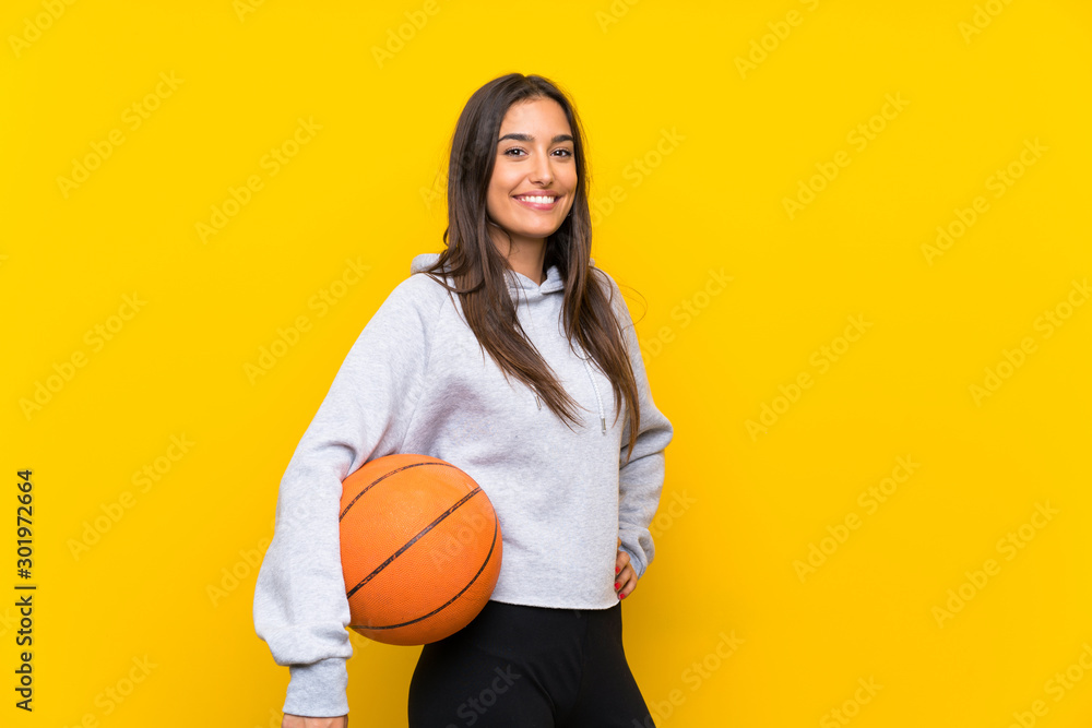 Young woman playing basketball over isolated yellow background Young woman playing basketball over isolated yellow background