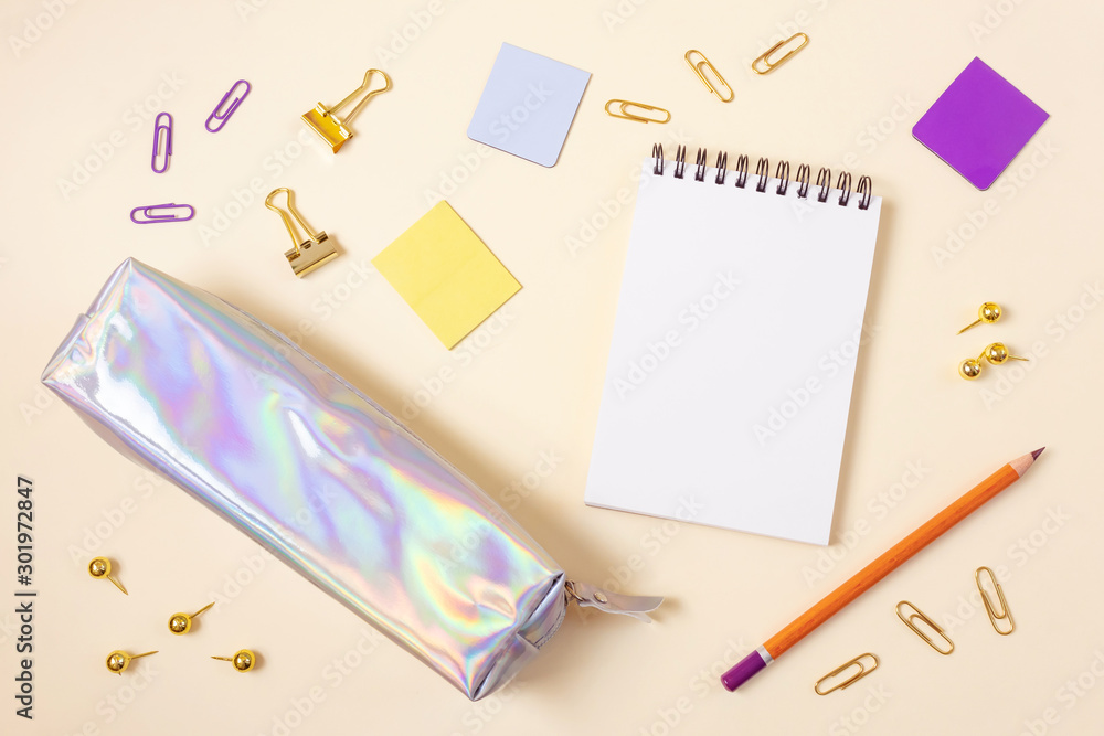 Pencil case, notebook on a spiral, golden paper clips, bookmarks, pencil, stickers on a light beige background. Place for text, minimalism. School, office, education concept. Pencil case, notebook on a spiral, golden paper clips, bookmarks, pencil, stickers on a light beige background. Place for text, minimalism. School, office, education concept.
