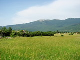Panorama of lush green vegetation on the outskirts of the village at the foot of a mountain ridge against the backdrop of a morning barely cloudy blue sky.