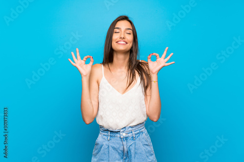 Young woman over isolated blue background in zen pose photo