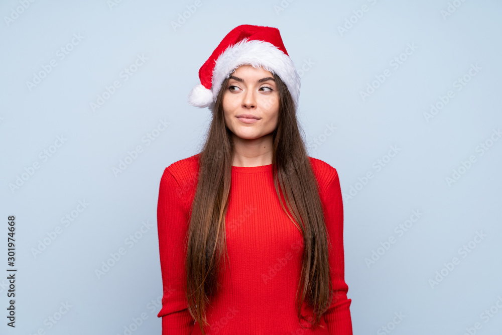 Girl with christmas hat over isolated blue background standing and looking to the side Girl with christmas hat over isolated blue background standing and looking to the side