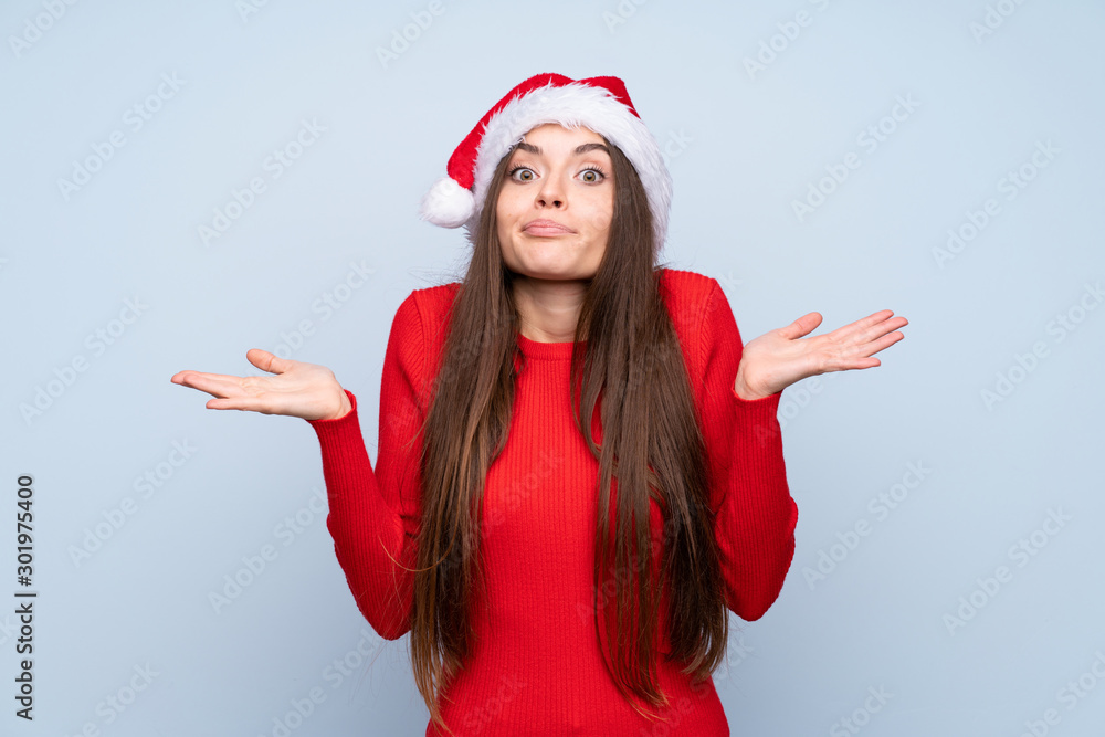 Girl with christmas hat over isolated blue background having doubts with confuse face expression Girl with christmas hat over isolated blue background having doubts with confuse face expression