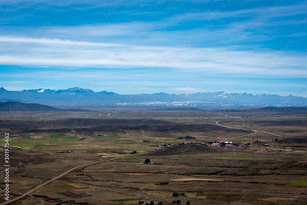 Crops surrounding the dry landscape on the outskirts of La Paz with the snow capped Cordillera Real Mountain Range in the distance on a cloudy day.