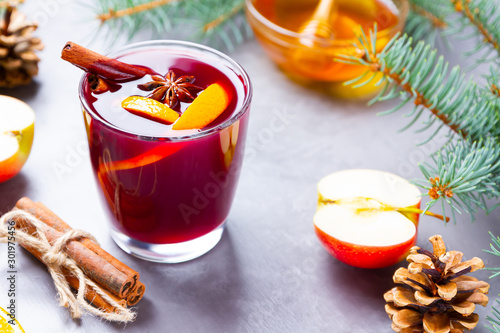 Mulled wine with spices in glass close up. Red mulled wine with cinnamon, anise and honey. Hot mulled wine at a cement gray background with fir branches and pine cones