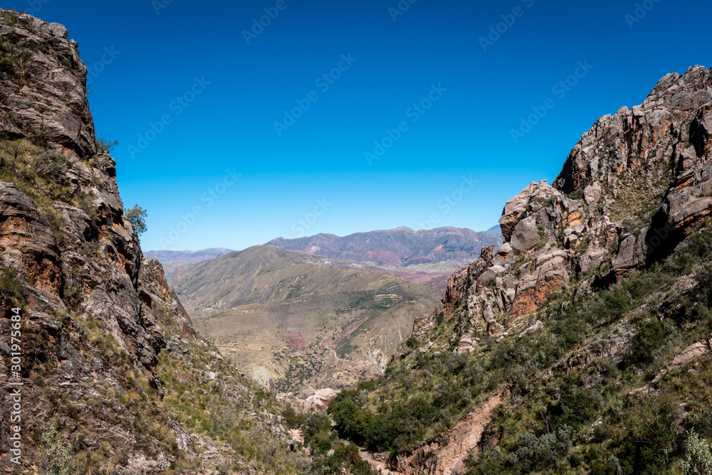 Fototapeta premium Crops surrounding the dry landscape on the outskirts of La Paz with the snow capped Cordillera Real Mountain Range in the distance on a cloudy day.