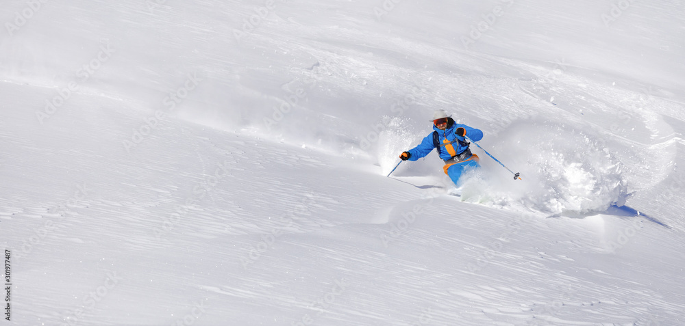 Skier skiing downhill in high mountains. professional rider in bright blue-orange ski suit and original hat on his head. snow-white background and place for text editing. Epic free ride scene