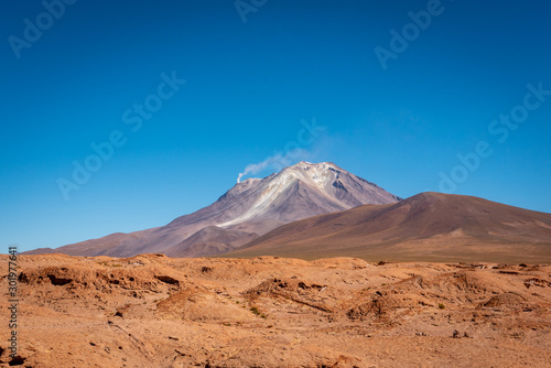 At the edge of Reserva Nacional de Fauna Andina Eduardo Avaroa, Putana Volcano lies on the border of Bolivia and Chile. Smoke streams from its crater flowing into the clear blue sky above.