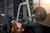Close view of charming a sporty woman in good shape lying on bench in modern fitness studio trying to start exercise with heavy barbell, preparing for competition of bodybuilders