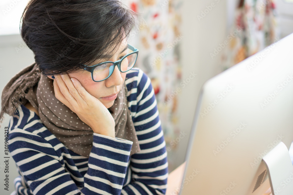 Smart looking middle aged Asian woman with blue light blocking glasses,  look at computer feeling tired. Computer Vision Syndrome (CVS) problem  concept - eye strain, dry, blurred, irritated, dizziness. Stock Photo
